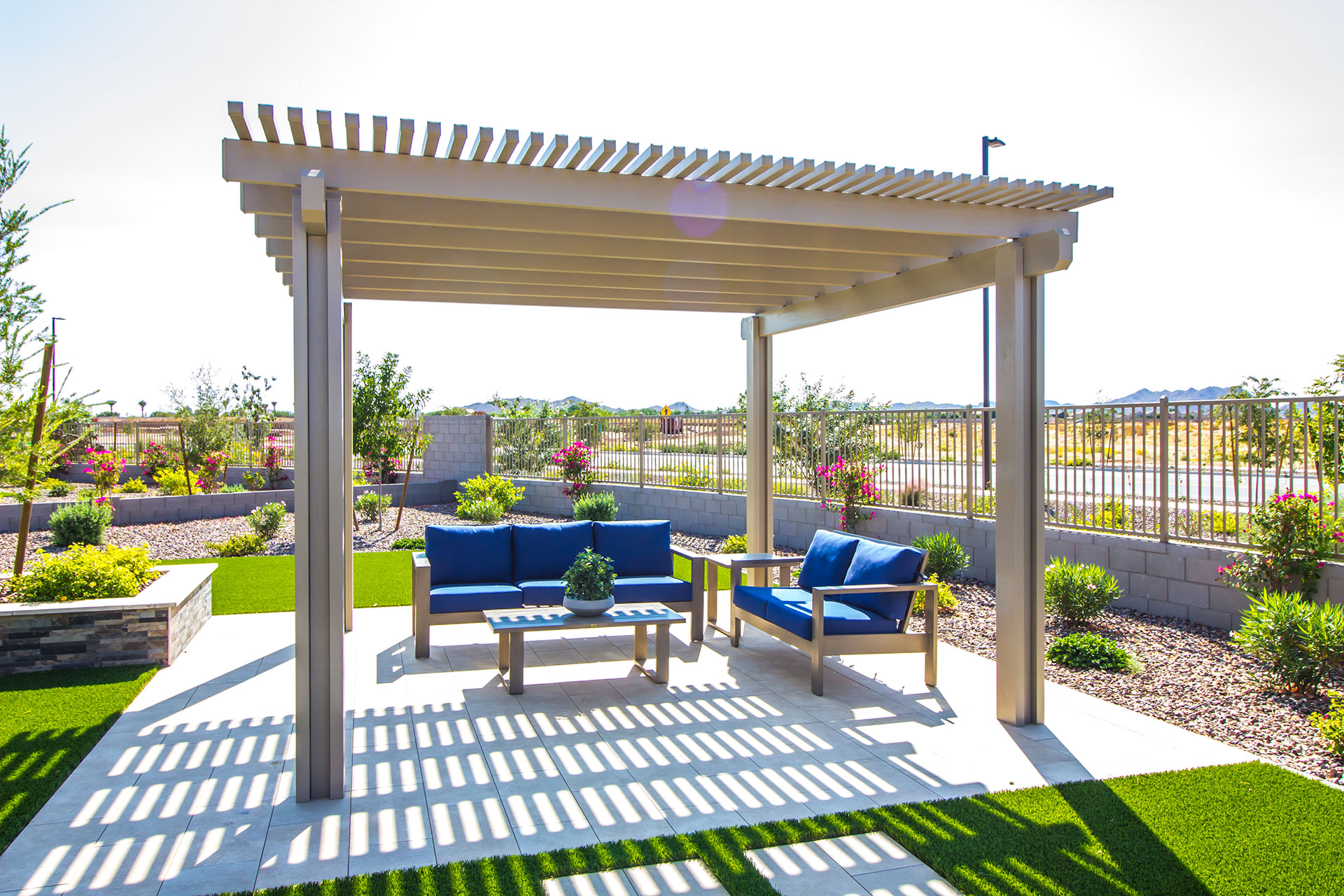 A detached pergola over a concrete patio with blue furniture.
